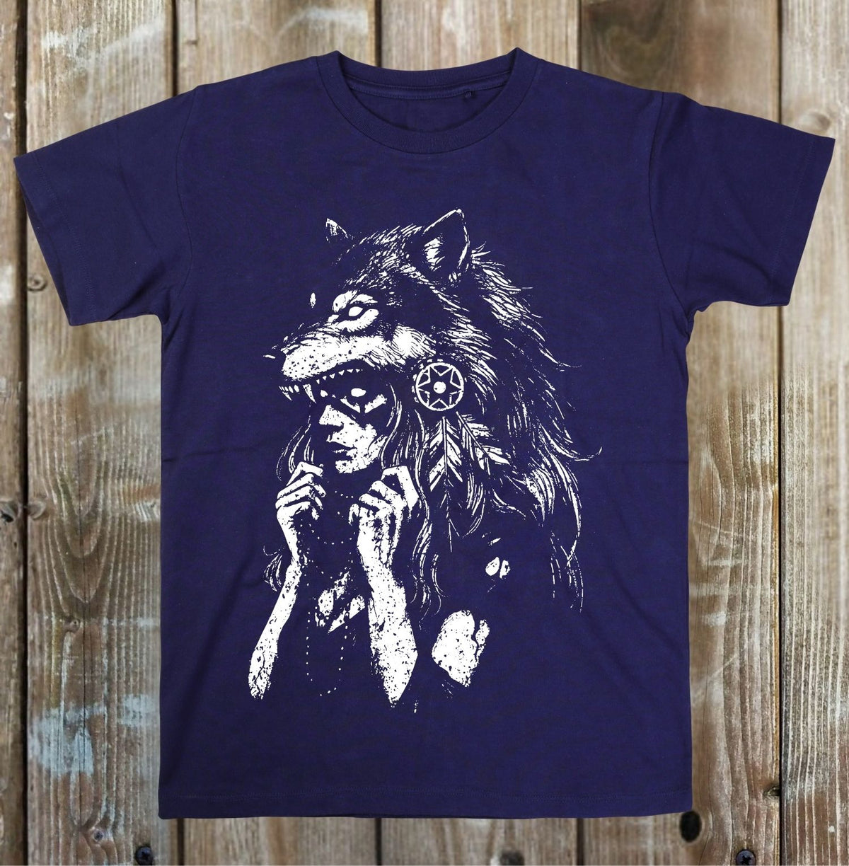A navy blue short-sleeve t-shirt with a distressed white graphic of a wolf-headed figure, displayed flat against a rustic wooden plank background.