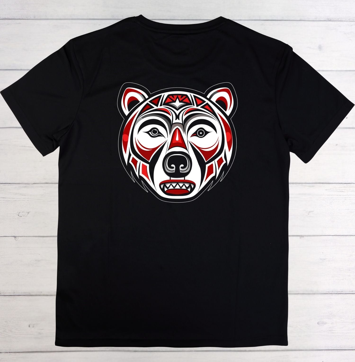 A black short-sleeve t-shirt laid flat on a white wood plank background, featuring a stylized red, white, and black bear head graphic on the chest.