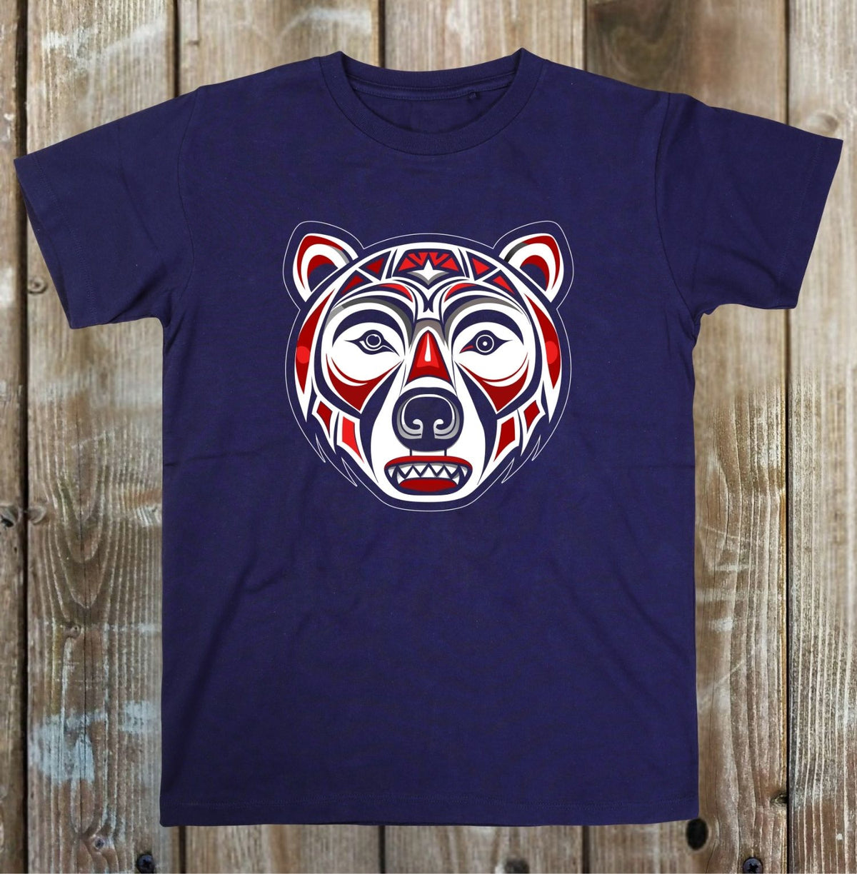 A navy blue short-sleeve t-shirt with a stylized, colorful bear head graphic in red, white, and blue, displayed flat against a rustic wooden plank background.