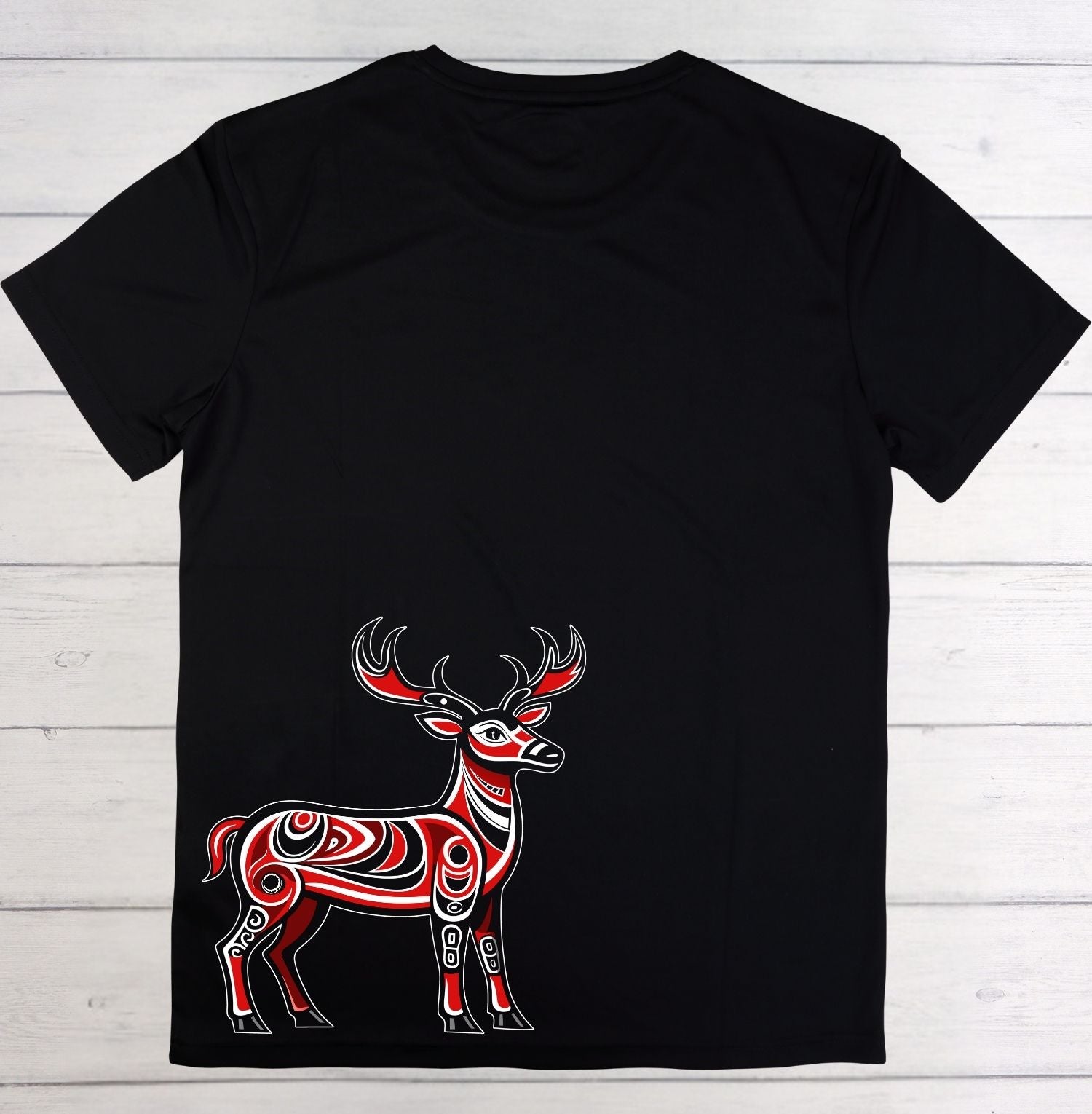 A black short-sleeve t-shirt laid flat on a white wood plank background, featuring a stylized red and white patterned deer graphic on the lower front.
