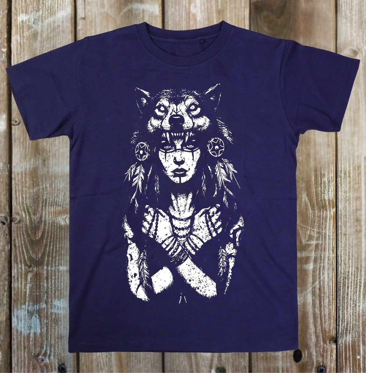 A navy blue short-sleeve t-shirt with a white distressed graphic of a woman with a wolf head, displayed flat against a rustic wooden plank background.