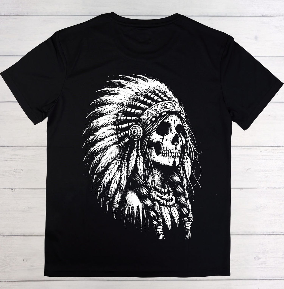 A black short-sleeve crewneck t-shirt featuring a large white graphic print of a skull wearing a feathered headdress, laid flat on a light gray wood plank background.