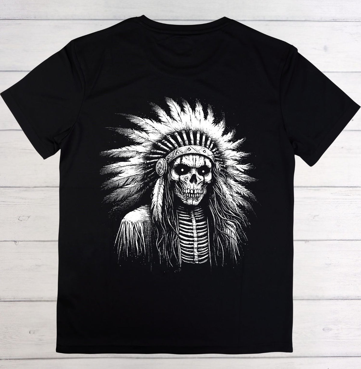 A black short-sleeve crewneck t-shirt featuring a large white graphic print of a skull wearing a feathered headdress, laid flat on a light gray wood plank background.