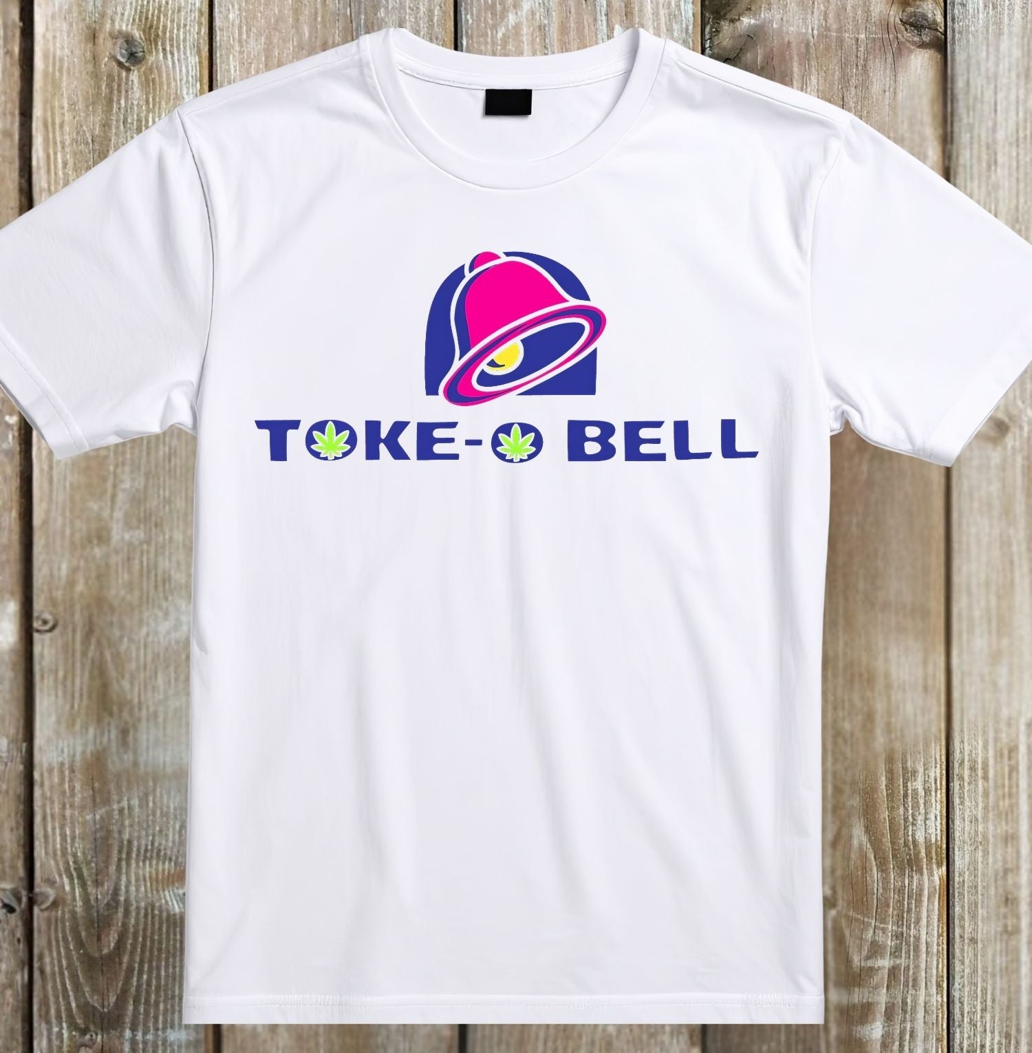 A white short-sleeve crewneck t-shirt laid flat on a rustic wooden plank background. The shirt features a graphic print on the chest with a pink and purple retro bell logo above the text 'TOKE-BELL' in blue, with green leaf icons replacing the 'O' characters.