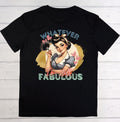 A black short-sleeve t-shirt laid flat on a white wood background, featuring a retro pin-up girl graphic with the text 'WHATEVER I'm still FABULOUS'.