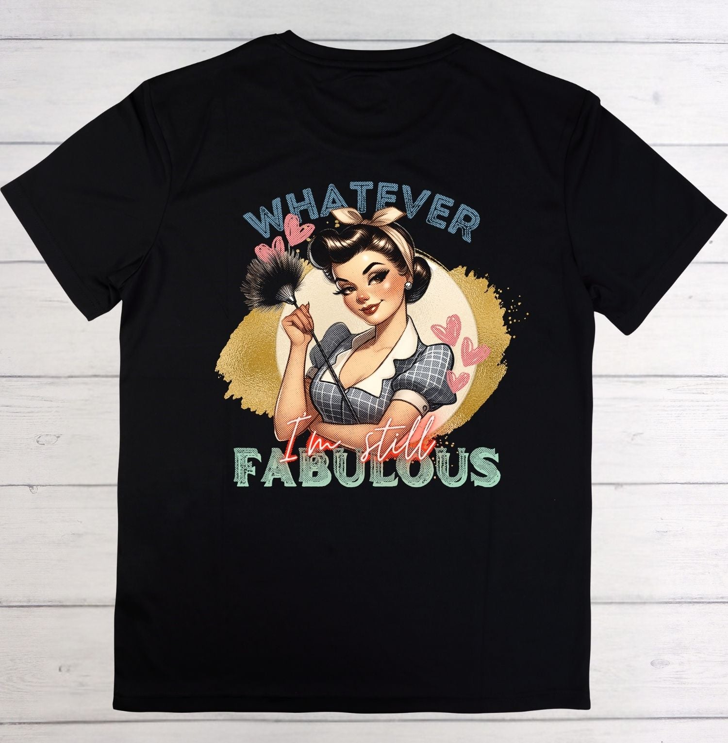 A black short-sleeve t-shirt laid flat on a white wood background, featuring a retro pin-up girl graphic with the text 'WHATEVER I'm still FABULOUS'.