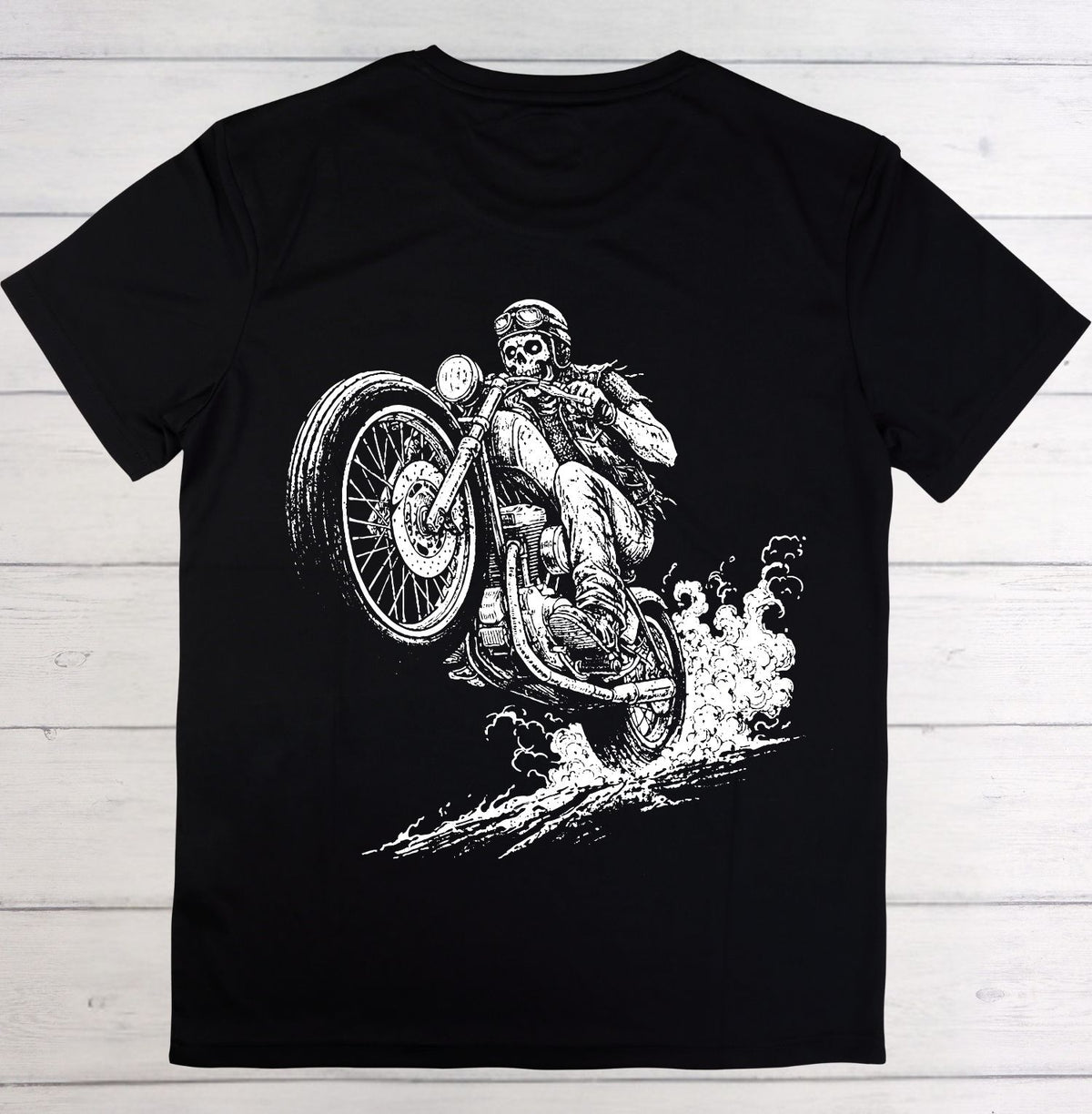 A black short-sleeve crewneck t-shirt laid flat on a light gray wood plank background, featuring a detailed white graphic print of a skeleton riding a motorcycle.