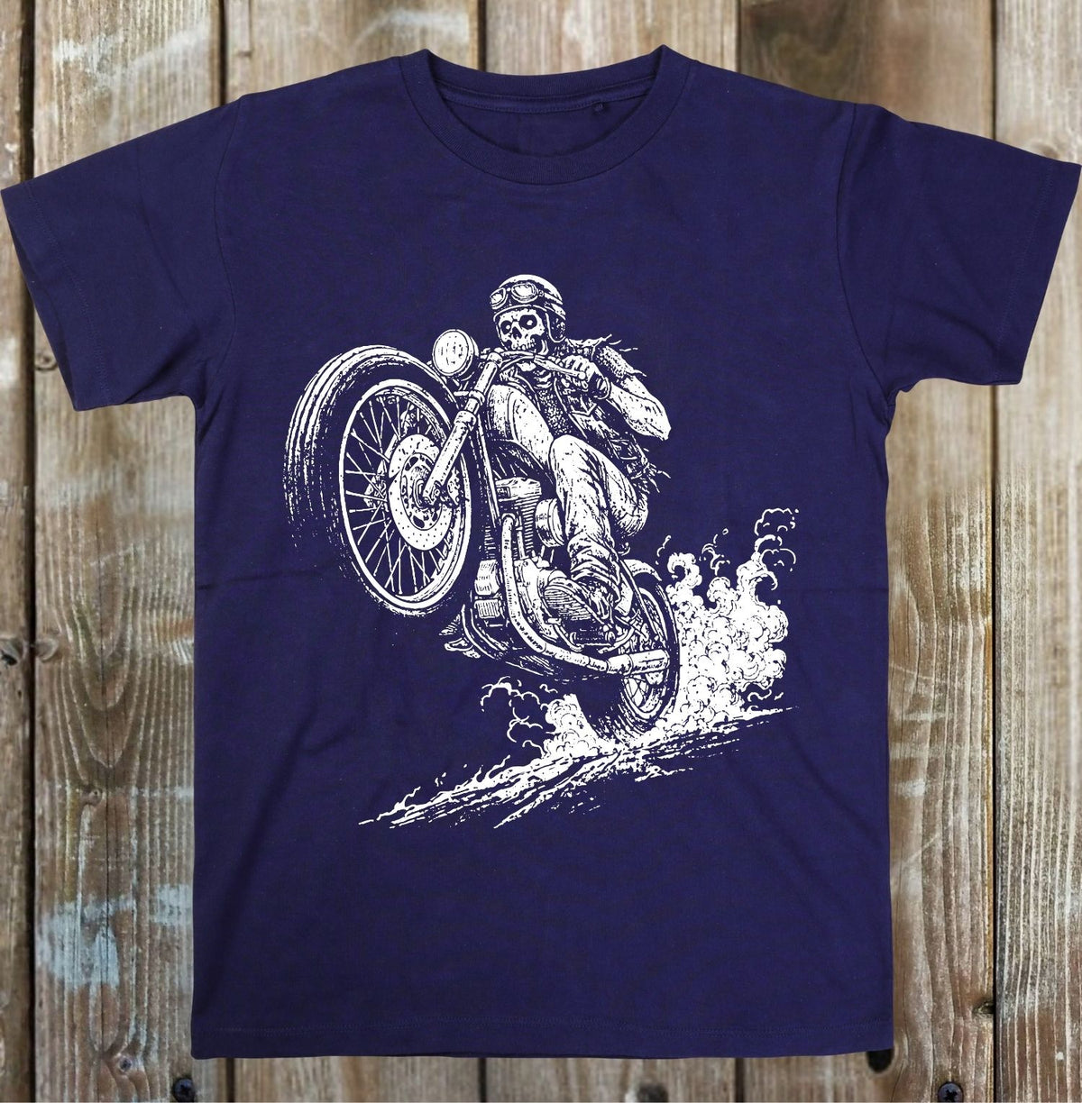 A blue short-sleeve crewneck t-shirt laid flat on a light gray wood plank background, featuring a detailed white graphic print of a skeleton riding a motorcycle.
