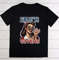 A black short-sleeve t-shirt with a retro-style graphic print featuring a woman in sunglasses and the text 'ZERO FU*KS GIVENS' in blue and red, displayed flat against a white wood plank background.