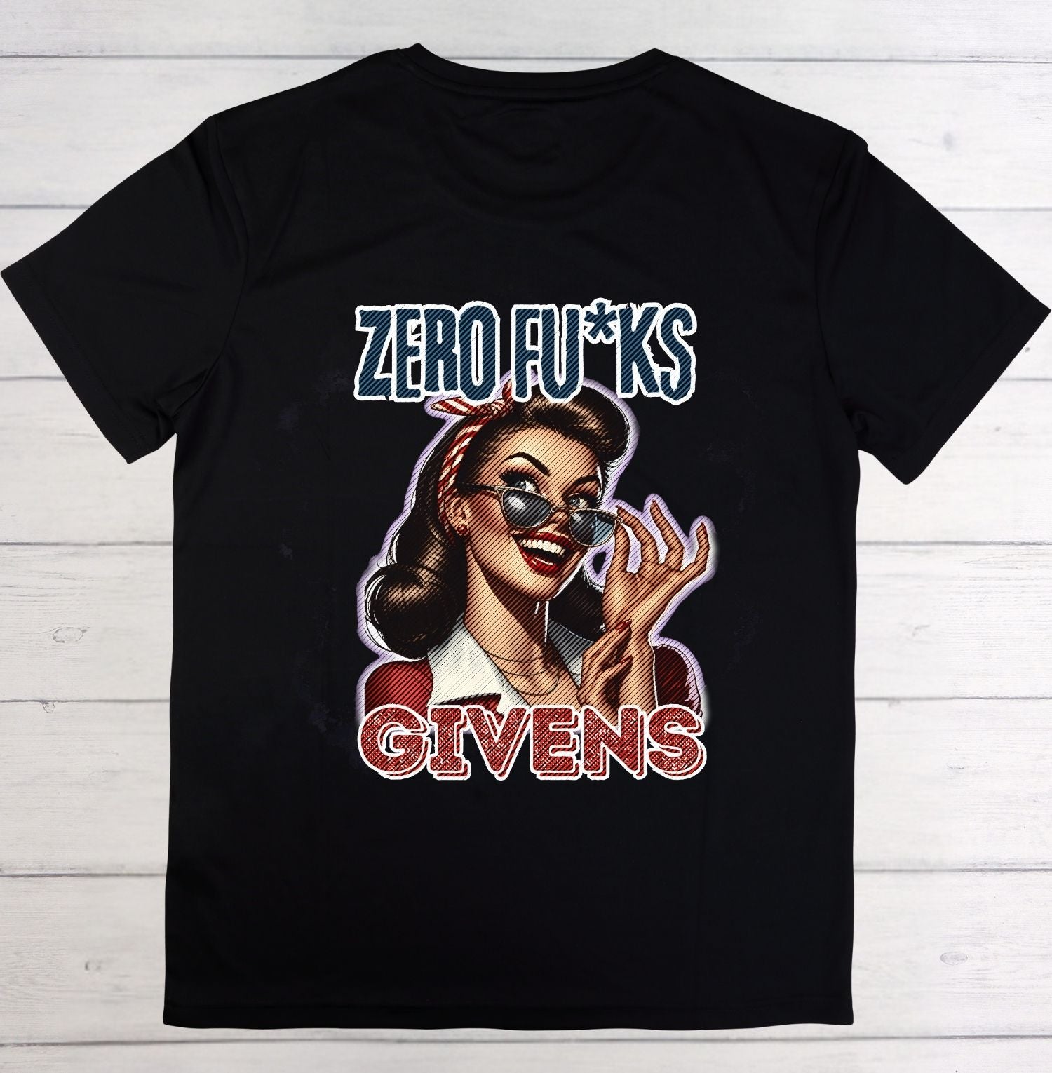 A black short-sleeve t-shirt with a retro-style graphic print featuring a woman in sunglasses and the text 'ZERO FU*KS GIVENS' in blue and red, displayed flat against a white wood plank background.
